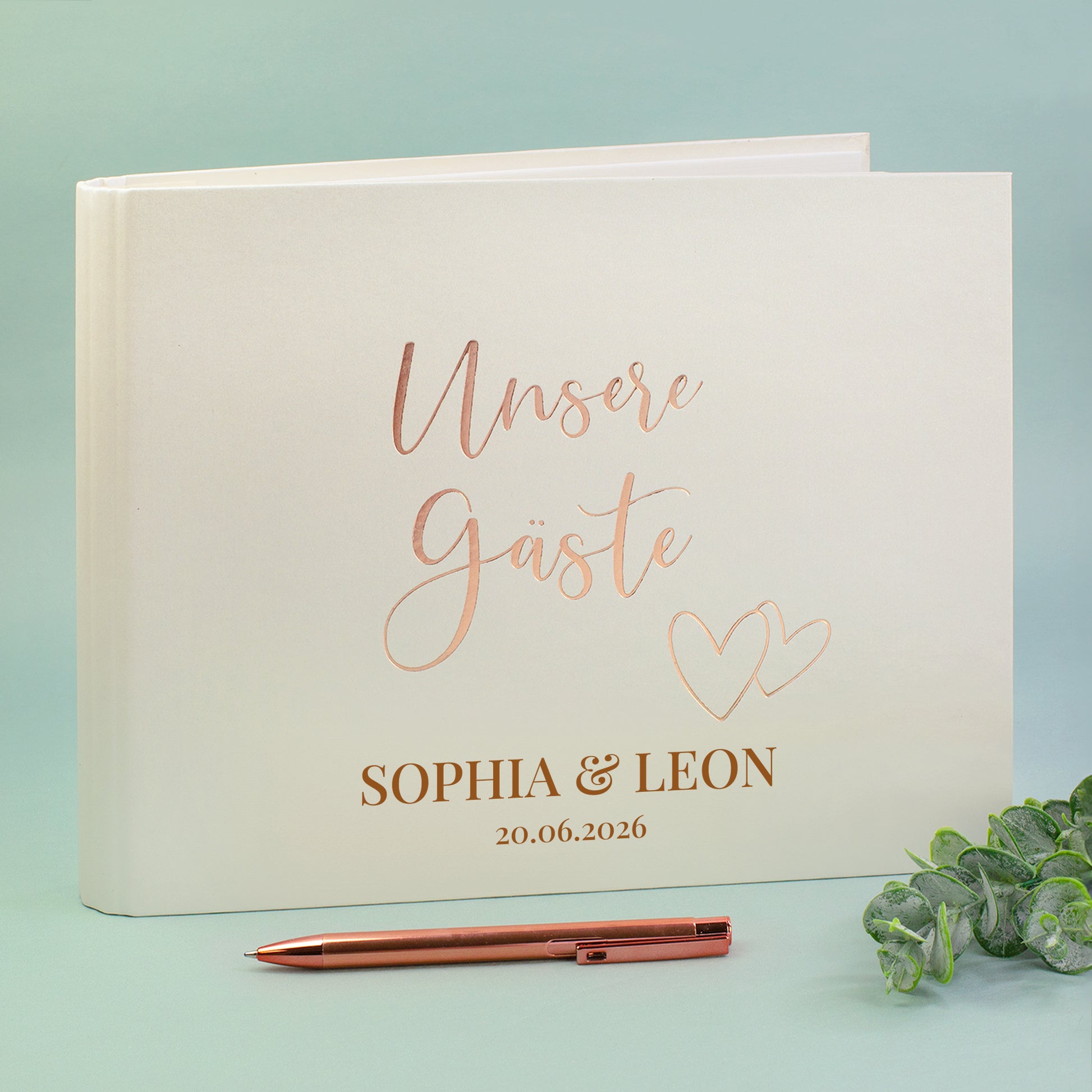 Gästebuch „Unsere Gäste“ mit Roségold-Prägung, personalisiert mit Namen Sophia & Leon und Hochzeitsdatum, Stift daneben.