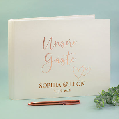 Gästebuch „Unsere Gäste“ mit Roségold-Prägung, personalisiert mit Namen Sophia & Leon und Hochzeitsdatum, Stift daneben.