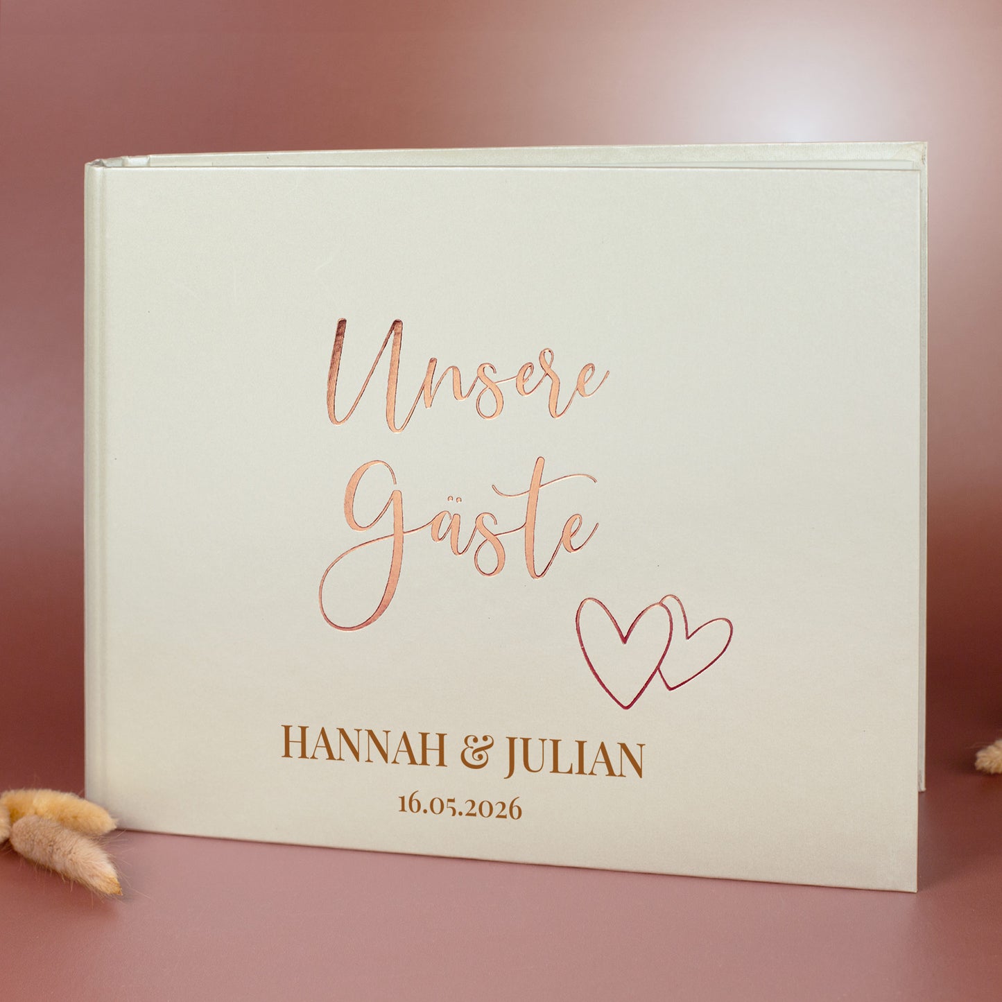 Gästebuch „Unsere Gäste“ mit Roségold-Schriftzug, personalisiert mit Namen Hannah & Julian und Hochzeitsdatum, vor braunem Hintergrund.