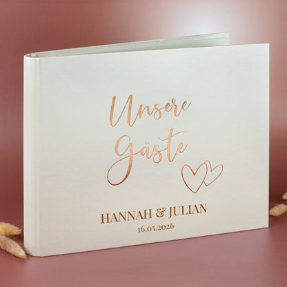 Gästebuch „Unsere Gäste“ mit Herzen und Personalisierung, Roségoldprägung auf cremefarbenem Einband.