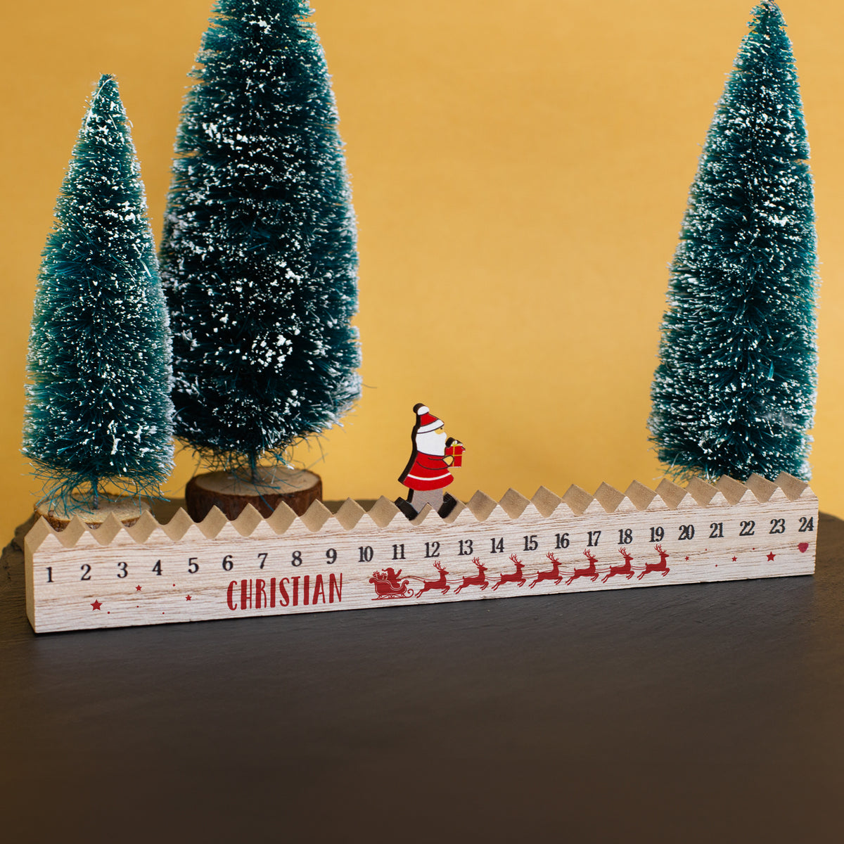 Walking-Santa-Adventskalender aus Holz mit personalisiertem Namen „Christian“ zwischen verschneiten Mini-Weihnachtsbäumen