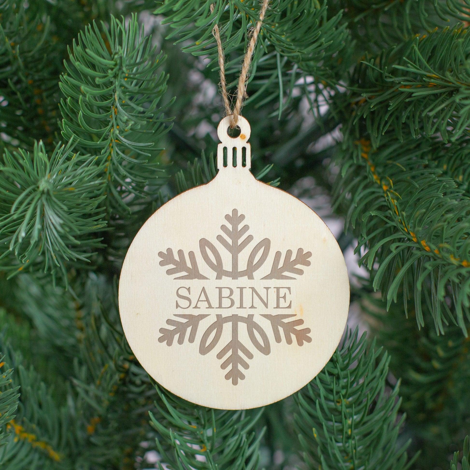 Weihnachtsbaumanhänger aus Holz, graviert und mit Juteschnur, als Christbaumschmuck dekoriert.