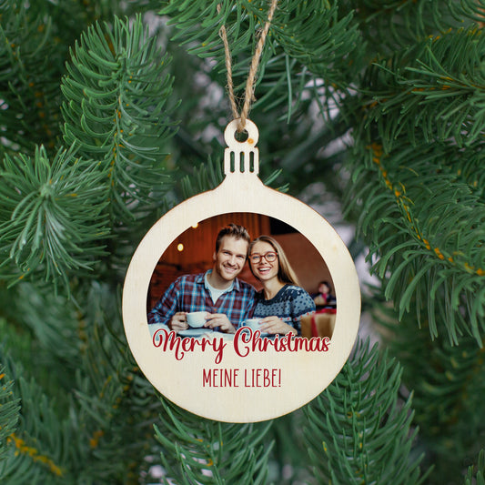 Personalisierter Christbaumanhänger mit Foto und Wunschtext – Holzanhänger „Merry Christmas“ mit roter Schrift, aufgehängt im Tannenbaum.