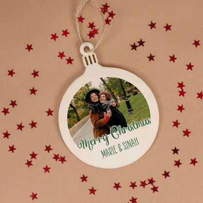 Weihnachtsanhänger aus Holz mit Foto zweier Freundinnen und grüner Aufschrift „Merry Christmas Marie & Sinah“ auf Tisch mit roten Sternen.