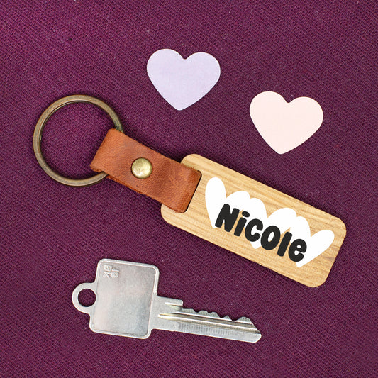 Personalisierter Schlüsselanhänger aus Holz mit Lederband und Metallring, bedruckt mit dem Namen Nicole und weißen Herzen auf violettem Hintergrund