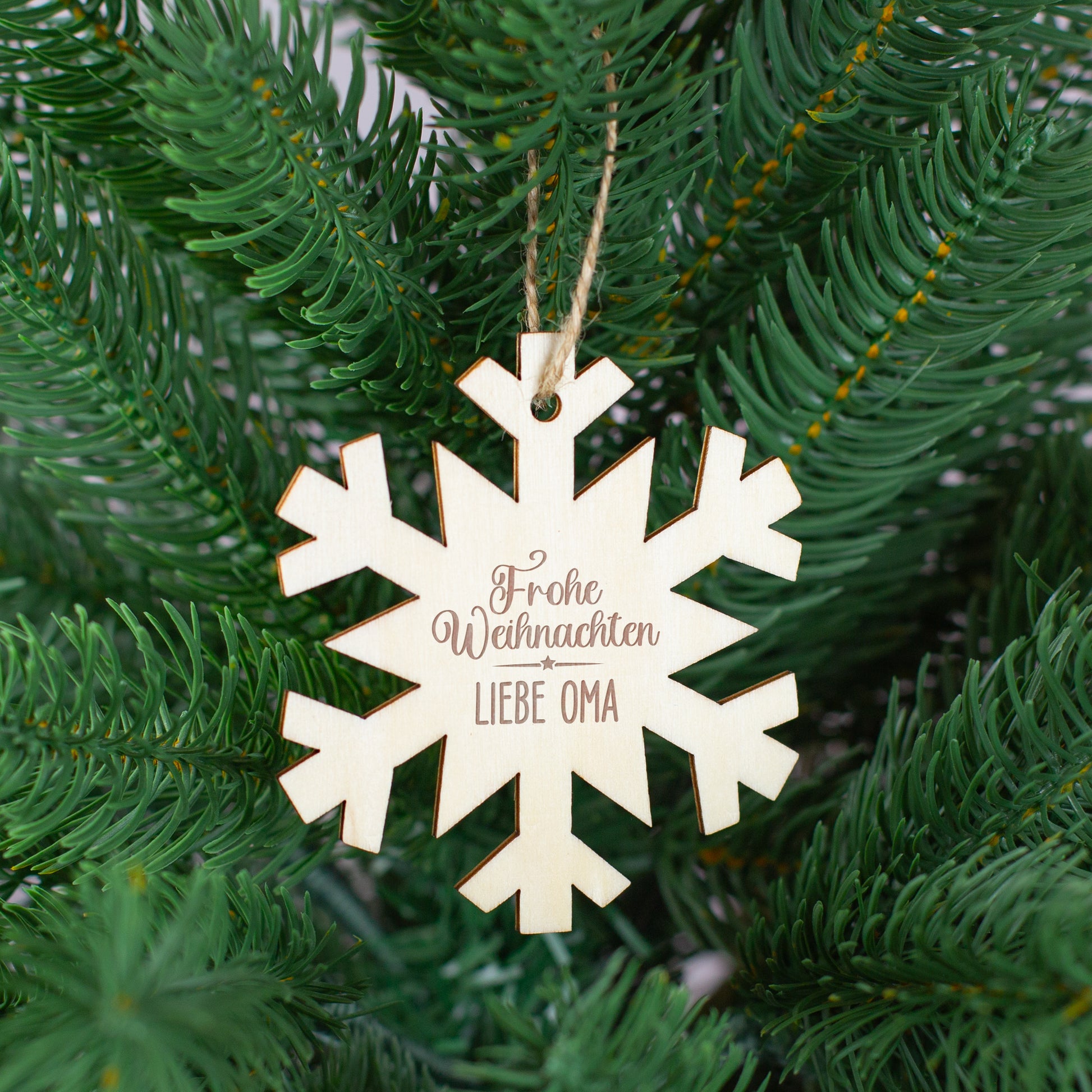 Schneeflocken-Anhänger aus Holz mit Gravur „Frohe Weihnachten Liebe Oma“, aufgehängt im Tannenbaum.