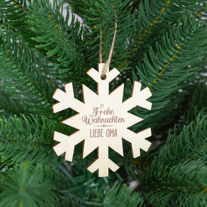 Schneeflocken-Anhänger aus Holz mit Gravur „Frohe Weihnachten Liebe Oma“, aufgehängt im Tannenbaum.
