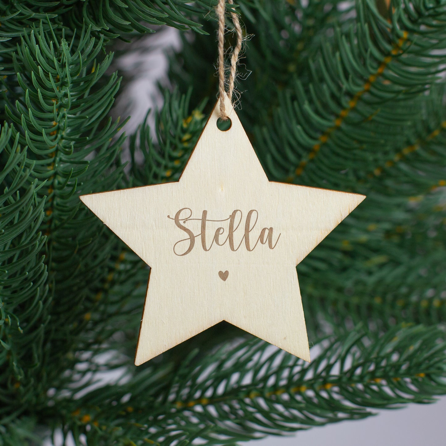 Personalisierter Sternanhänger aus Holz mit Gravur „Stella“ und Herz, aufgehängt im Weihnachtsbaum.
