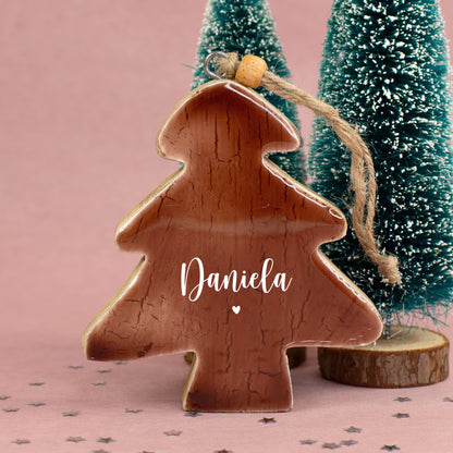 Personalisierter Weihnachtsbaum-Anhänger aus Holz mit dem Namen Daniela und kleinem Herz vor winterlicher Weihnachtsdekoration