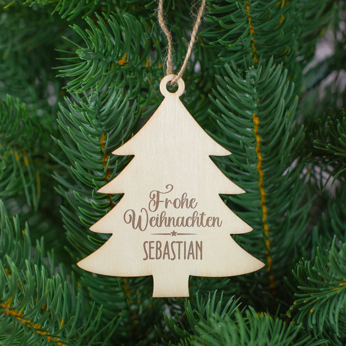 Tannenbaum-Anhänger aus Holz mit Gravur „Frohe Weihnachten Sebastian“, aufgehängt im grünen Christbaum.
