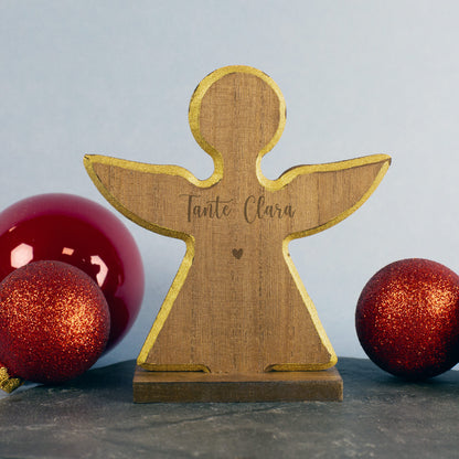 Holzengel mit ausgebreiteten Flügeln und Gravur „Tante Clara“ unter einem kleinen Herz, flankiert von zwei roten Weihnachtskugeln.