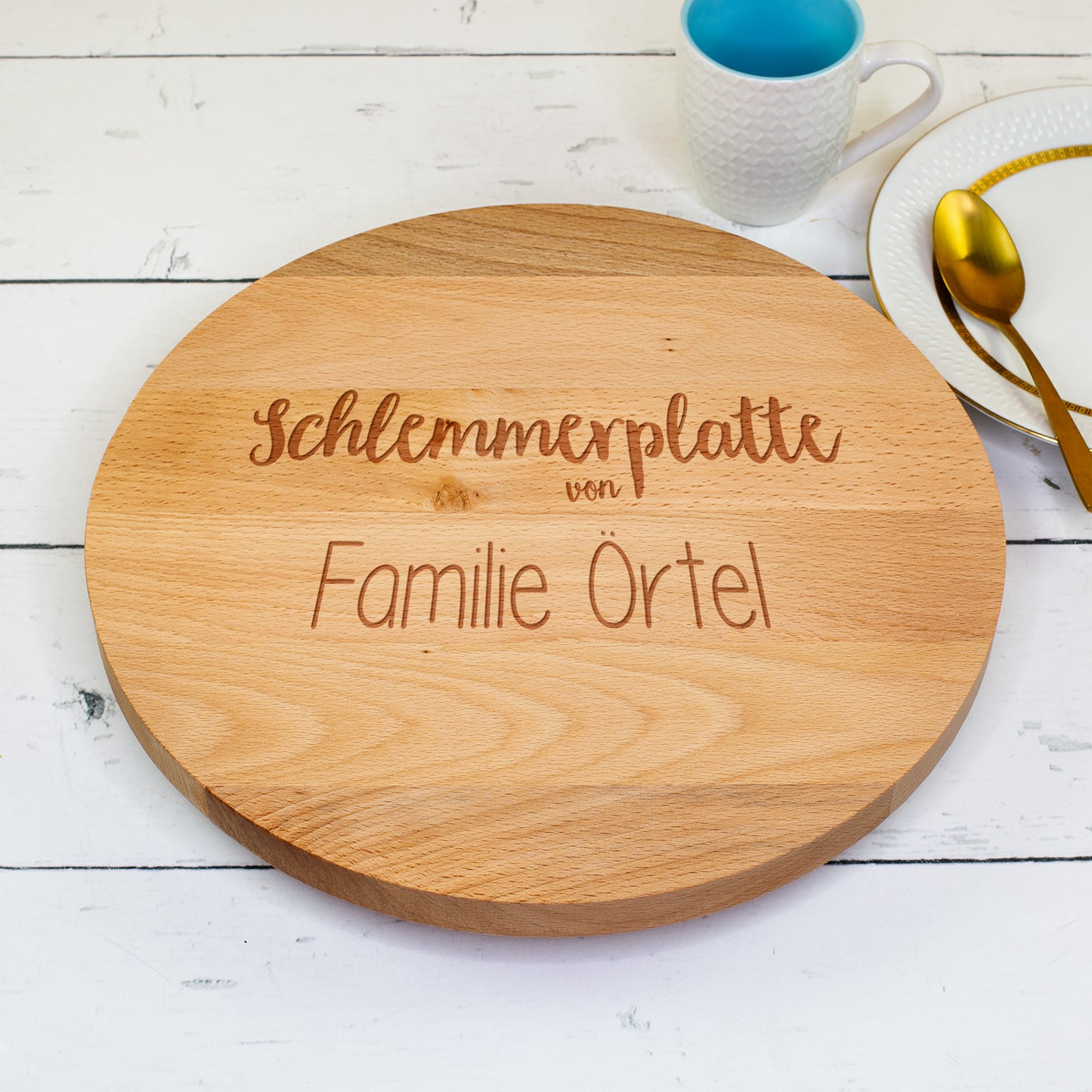 Servierplatte aus Buchenholz mit Gravur „Schlemmerplatte von Familie Örtel“, arrangiert neben Teller und Tasse