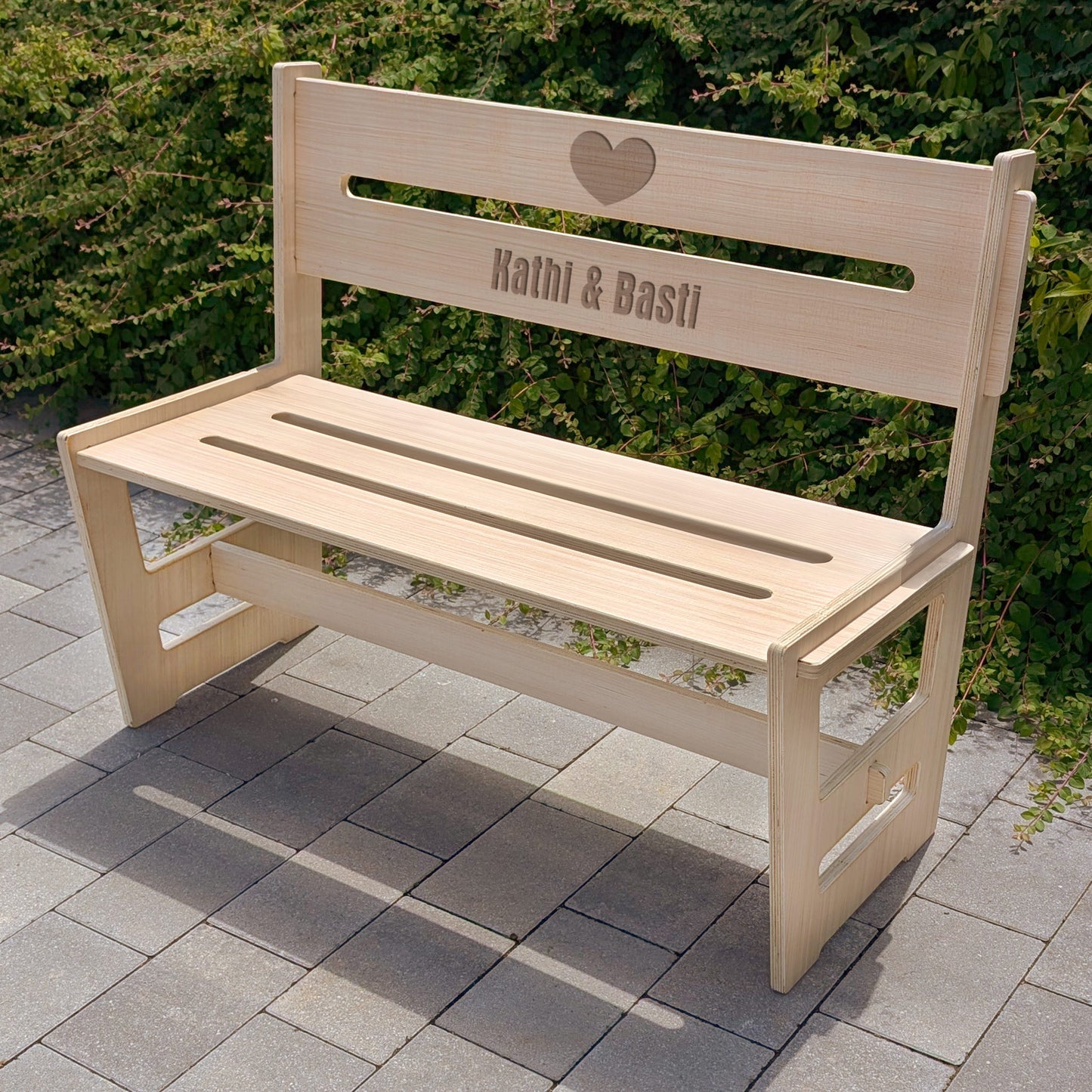 Holzbank mit Gravur „Kathi & Basti“ und Herzsymbol, aufgestellt im Garten – romantische Sitzgelegenheit für draußen