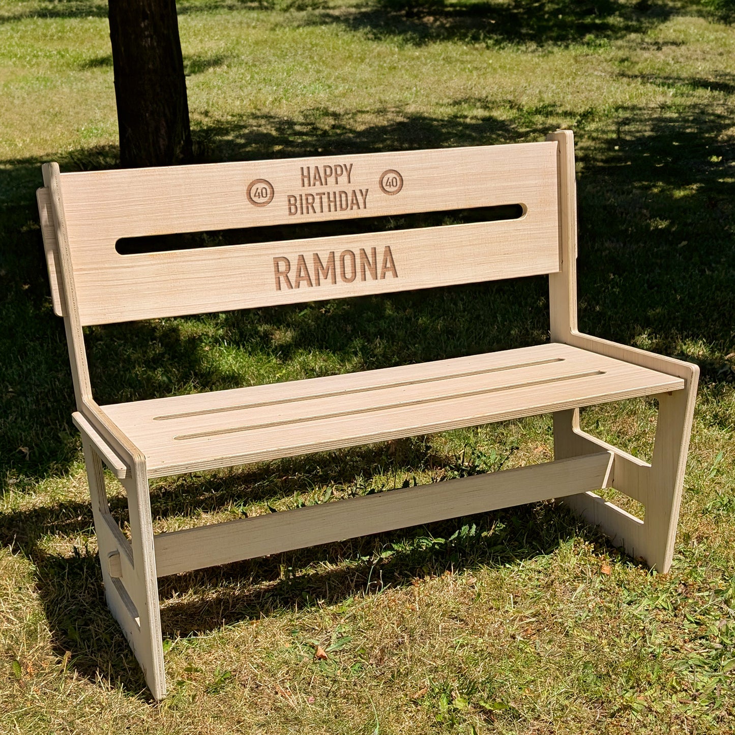 Personalisierte Holzbank mit Gravur 'Happy Birthday Ramona' auf einer Wiese im Sonnenschein – ideal als Geschenk zum Geburtstag
