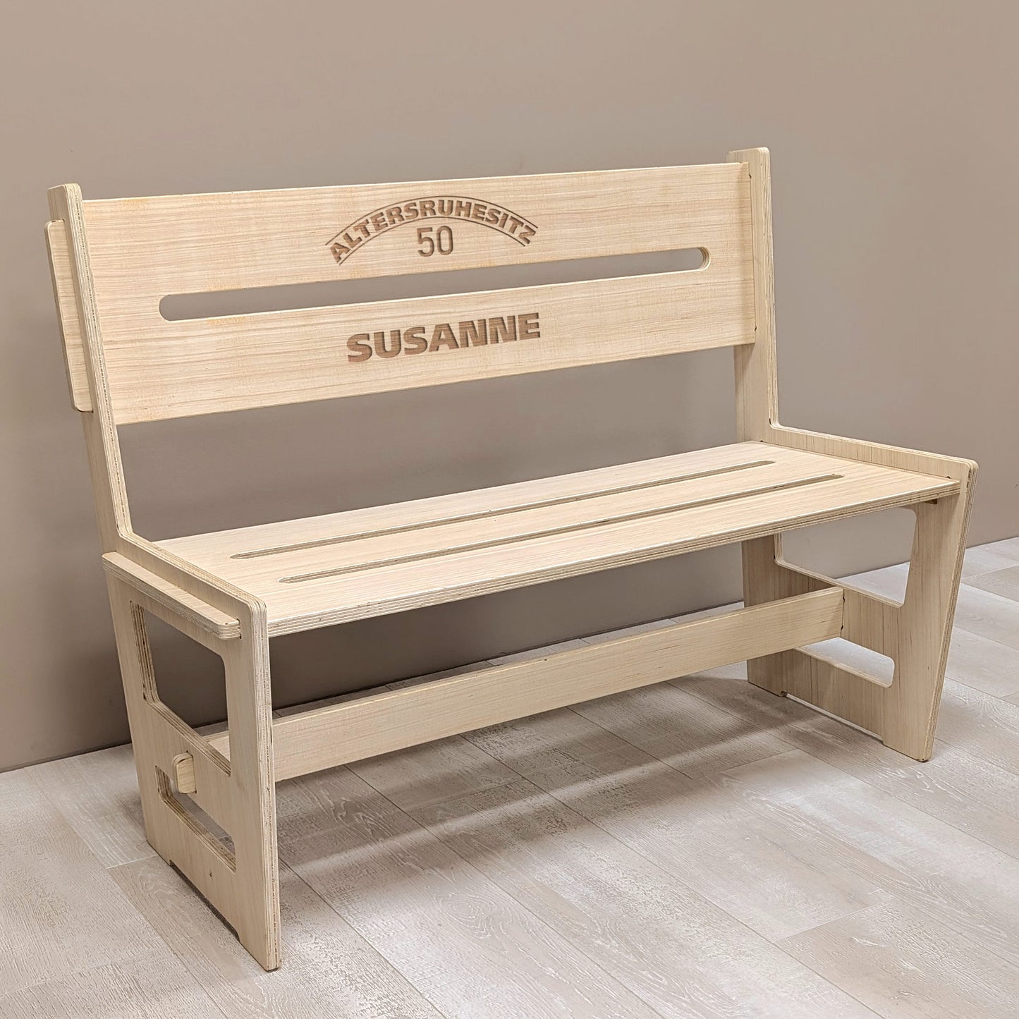 Personalisierte Holzbank für den Ruhestand mit Gravur „Altersruhesitz 50 SUSANNE“ in Innenraumkulisse