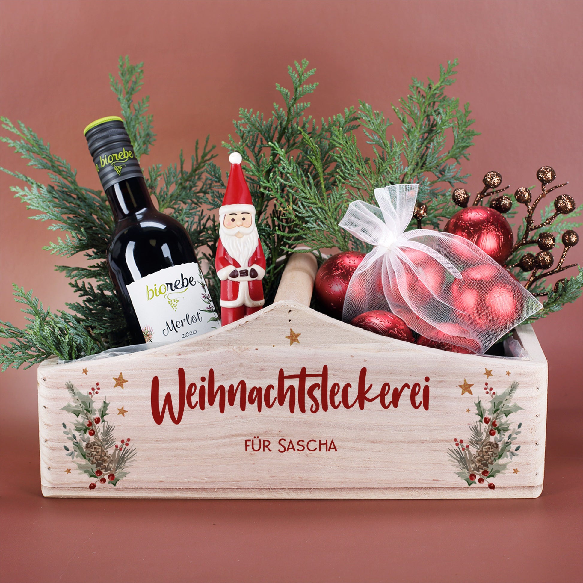 Gefüllter Weihnachtskorb mit Winterbouquet-Motiv, roten Kugeln, Wein und Tannengrün als Geschenkarrangement.