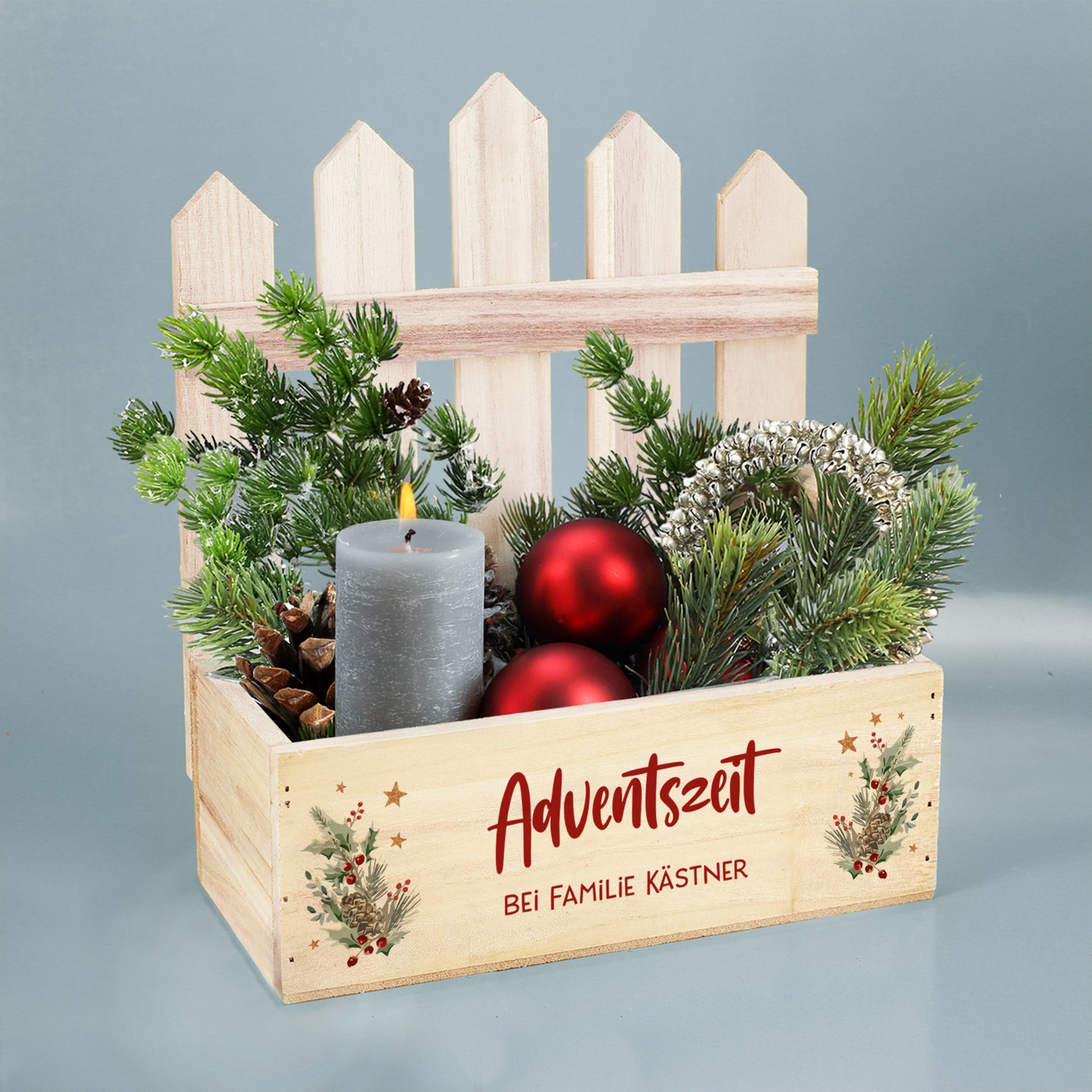 Winterliche Pflanzkiste mit Zaun, Tannenzweigen, Zapfen und roten Kugeln als Adventsdekoration