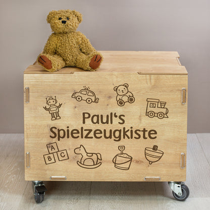 Personalisierte Holz-Rollkiste mit Deckel und Rollen, Vorderseite mit graviertem Namen „Paul“ und Spielzeugmotiven wie Roboter, Auto, Teddy und Bauklötzen