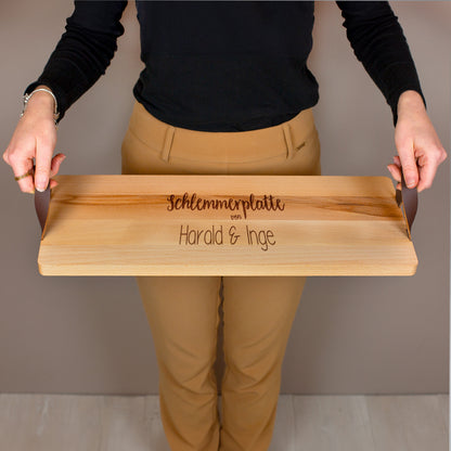 Servierbrett mit Ledergriffen im Einsatz, getragen von einer Person, Gravur „Schlemmerplatte von Harald & Inge“.