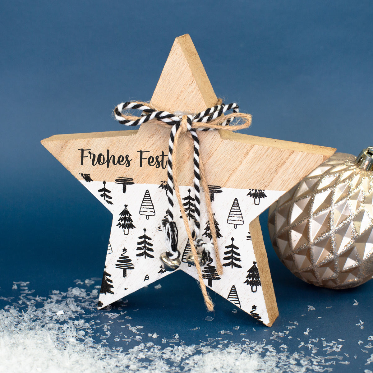 Holzstern mit Aufdruck „Frohes Fest“, Glöckchen und schwarz-weißem Weihnachtsbaum-Muster in winterlicher Dekoration