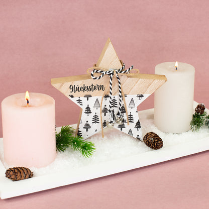 Personalisierter Holzstern „Glücksstern“ mit schwarz-weißem Tannenbaum-Motiv und Glöckchen zwischen zwei Weihnachtskerzen