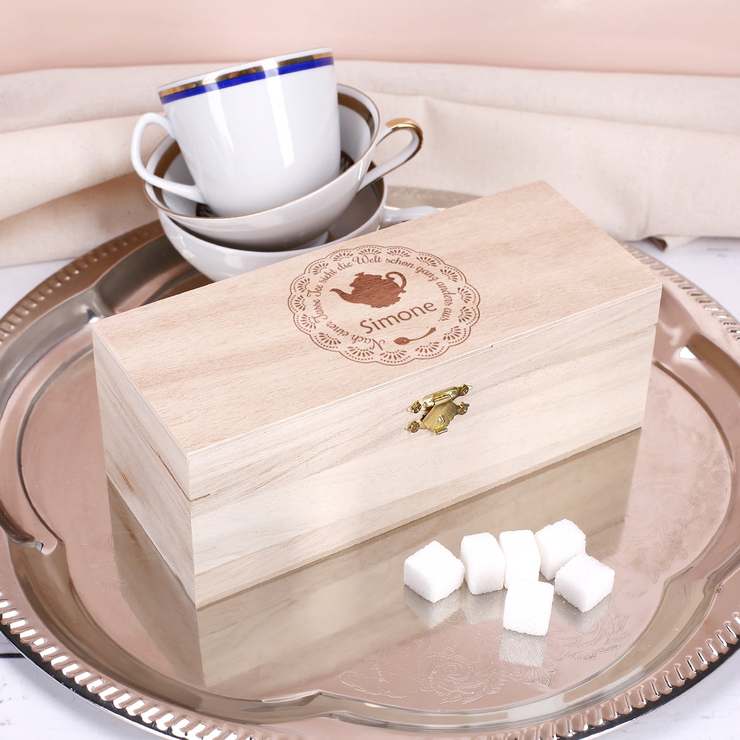 Gravierte Teebox aus Holz mit Spruch „Nach einer Tasse Tee sieht die Welt schon ganz anders aus“ und Name Simone auf silbernem Tablett mit Teetassen.