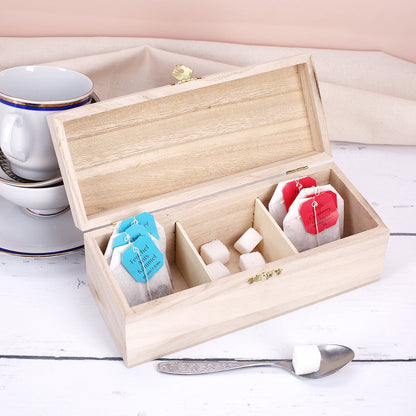 Offene Teebox aus Holz mit drei Fächern, befüllt mit Teebeuteln und Zuckerwürfeln auf hellem Tisch.
