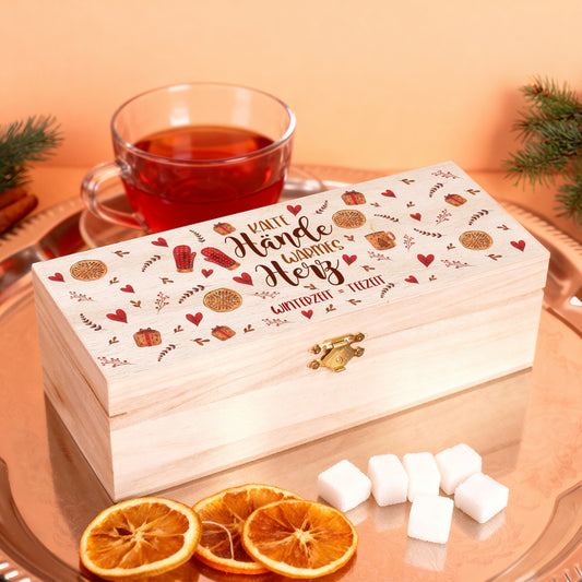 Personalisierte Teebox mit Gravur „Kalte Hände, warmes Herz – Winterzeit = Teezeit“, arrangiert auf einem Tablett mit Teetasse, Zuckerwürfeln und getrockneten Orangenscheiben, warmes Licht.