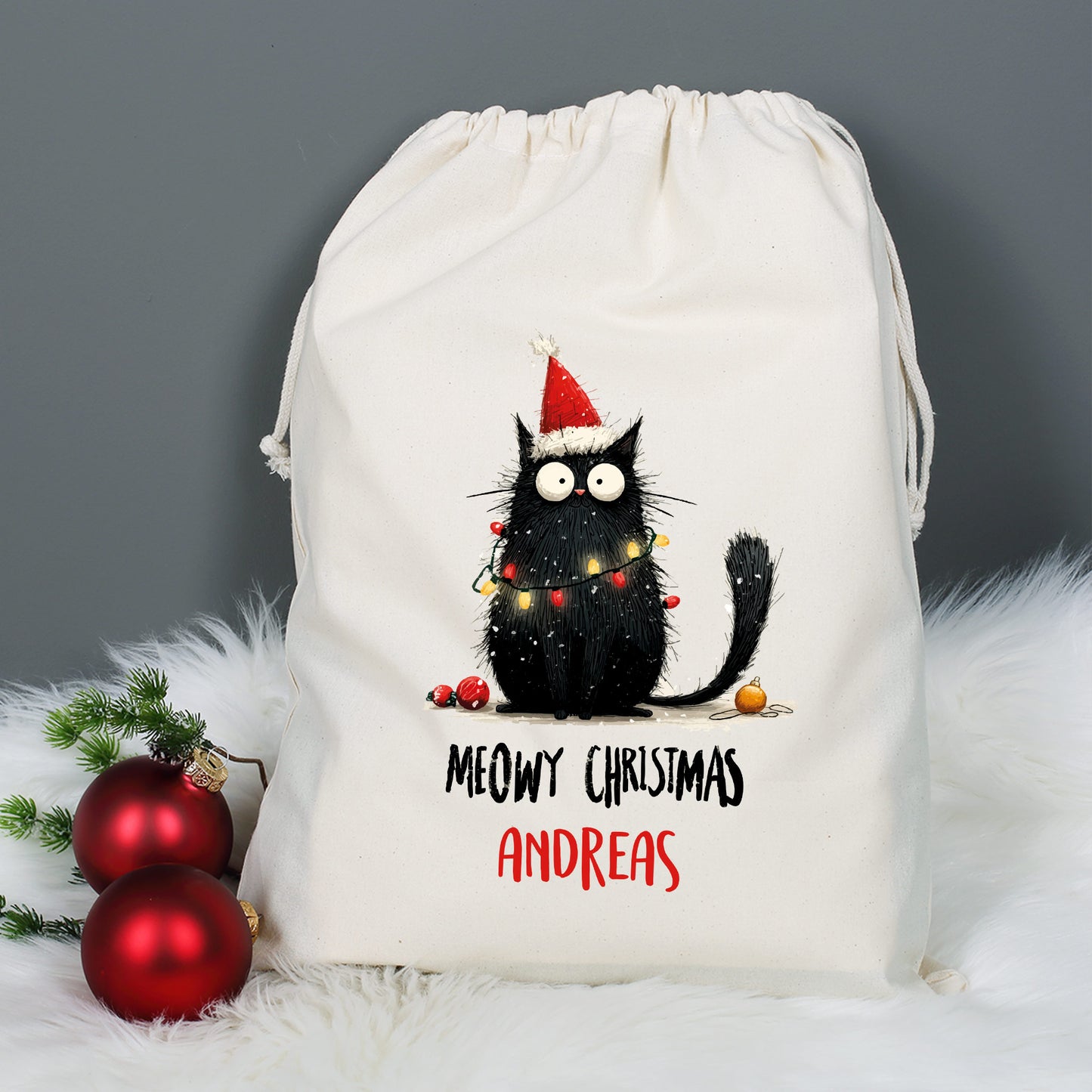 Großer Geschenksack mit Aufdruck „Meowy Christmas – Andreas“ vor weihnachtlicher Dekoration mit roten Kugeln