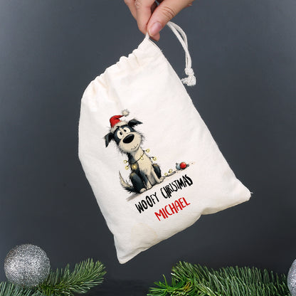 Kleiner Baumwollbeutel mit Hund in Weihnachtsmütze und Aufdruck „Woofy Christmas – Michael“, gehalten von einer Hand