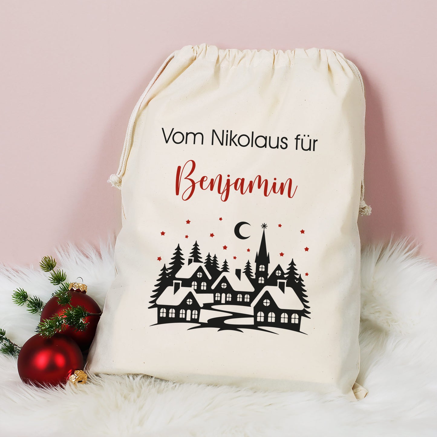 Großer Baumwoll-Geschenksack mit Aufdruck „Vom Nikolaus für Benjamin“ und Winterlandschaft, dekoriert mit Christbaumkugeln auf weißem Fell.