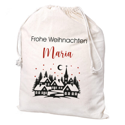 Freigestellter großer Baumwollbeutel mit Winterdorf-Motiv und Wunschtext „Frohe Weihnachten Maria“, rote Akzente und Kordelzug sichtbar.
