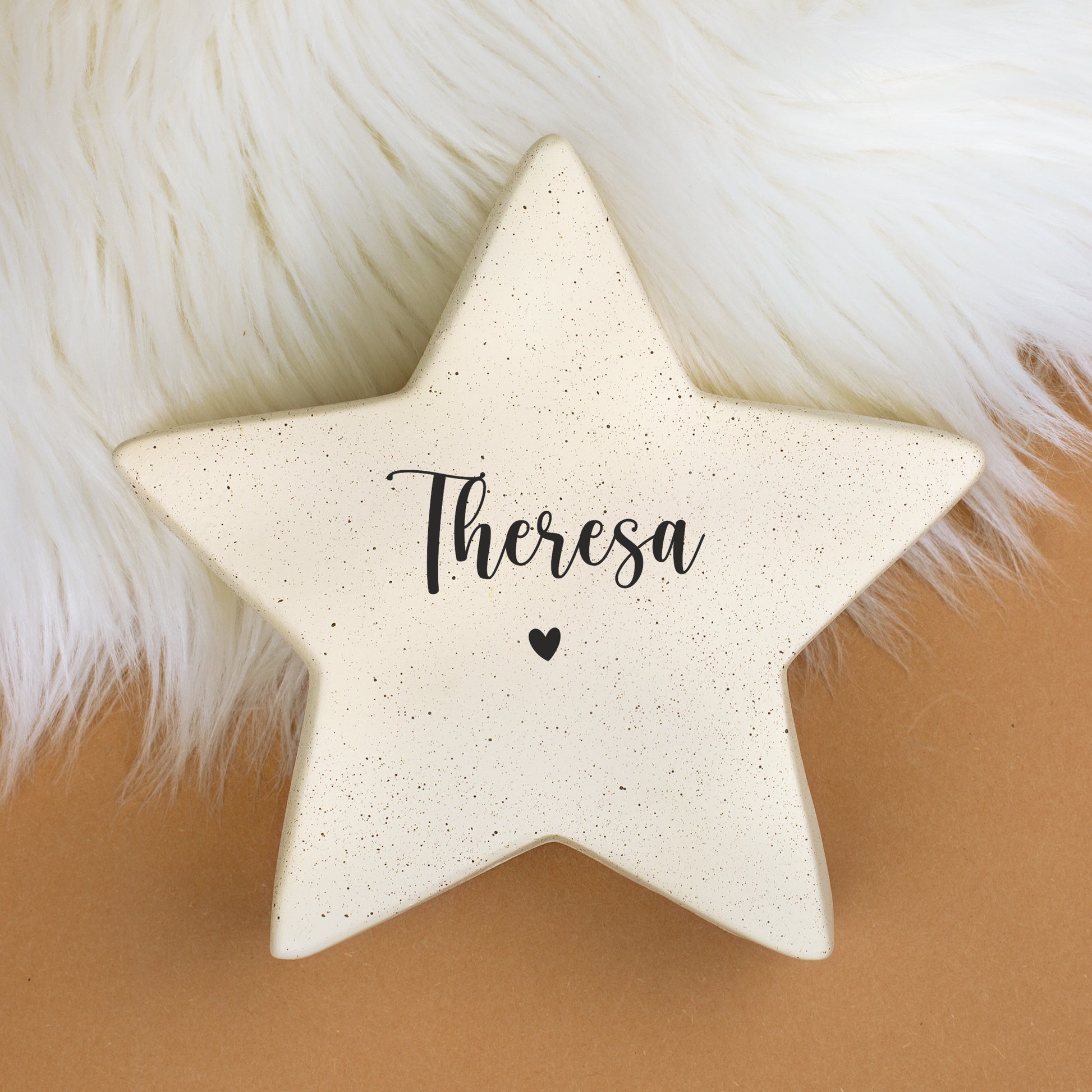 Cremefarbener Keramikstern mit Namensaufdruck „Theresa“ und Herzmotiv auf weißem Fellhintergrund.