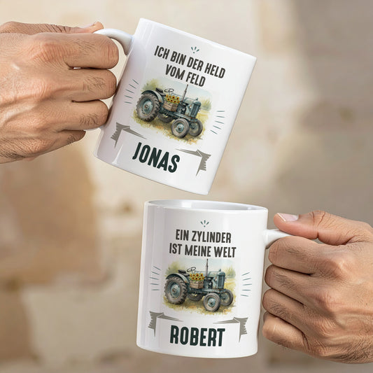 Zwei Retro-Traktor-Tassen in Händen, mit den Aufdrucken „Ich bin der Held vom Feld“ und „Ein Zylinder ist meine Welt“, personalisiert mit Jonas und Robert