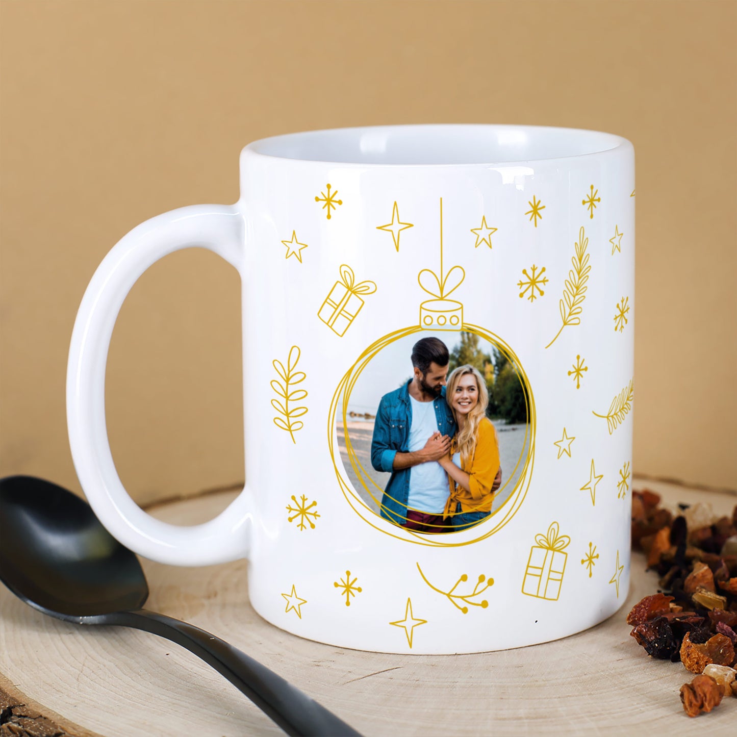 Weiße Tasse mit goldgelbem Weihnachtskugel-Design und Pärchenfoto, dekoriert mit Sternen und Zweigen.