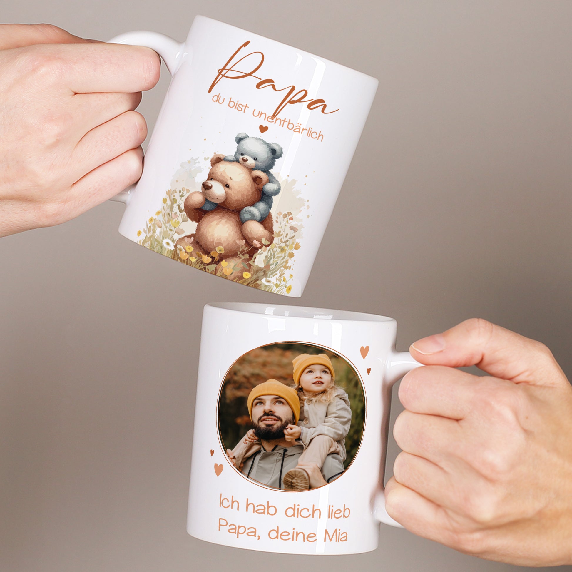 Zwei weiße Tassen werden in den Händen gehalten, links mit Bärenmotiv und dem Spruch „Papa du bist unentbärlich“, rechts mit personalisiertem Foto und Text für Papa.