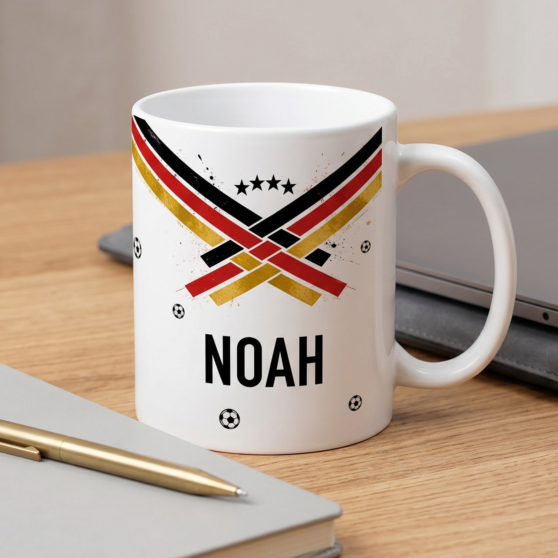 Fußball Tasse mit Name Noah, sportliches Schwarz-Rot-Gold-Motiv mit Sternen, neben Notizbuch und Stift auf dem Schreibtisch