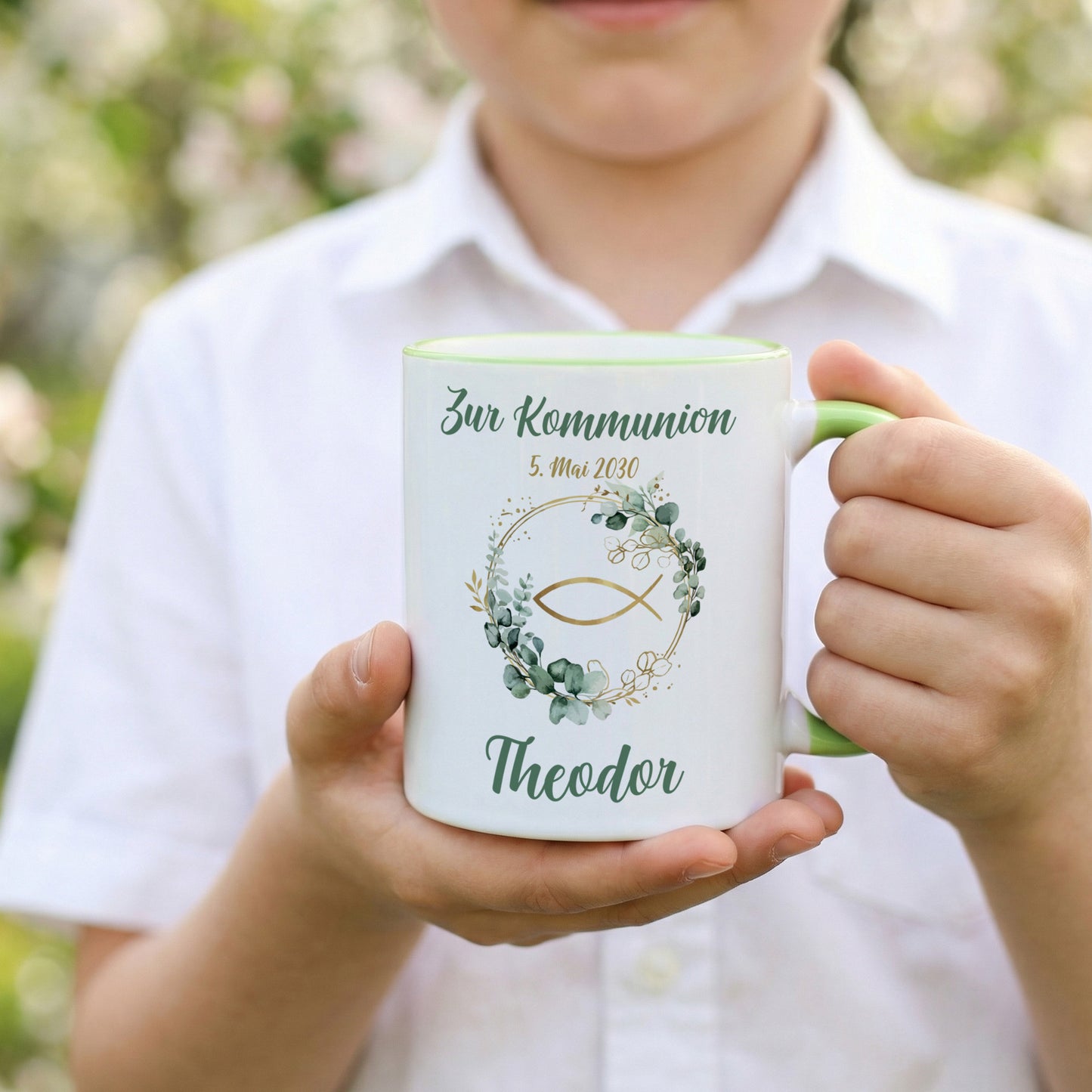Kind hält personalisierte Kommunionstasse mit Ichthys-Fisch, Eukalyptusmotiv und Name „Theodor“ sowie Datum in den Händen