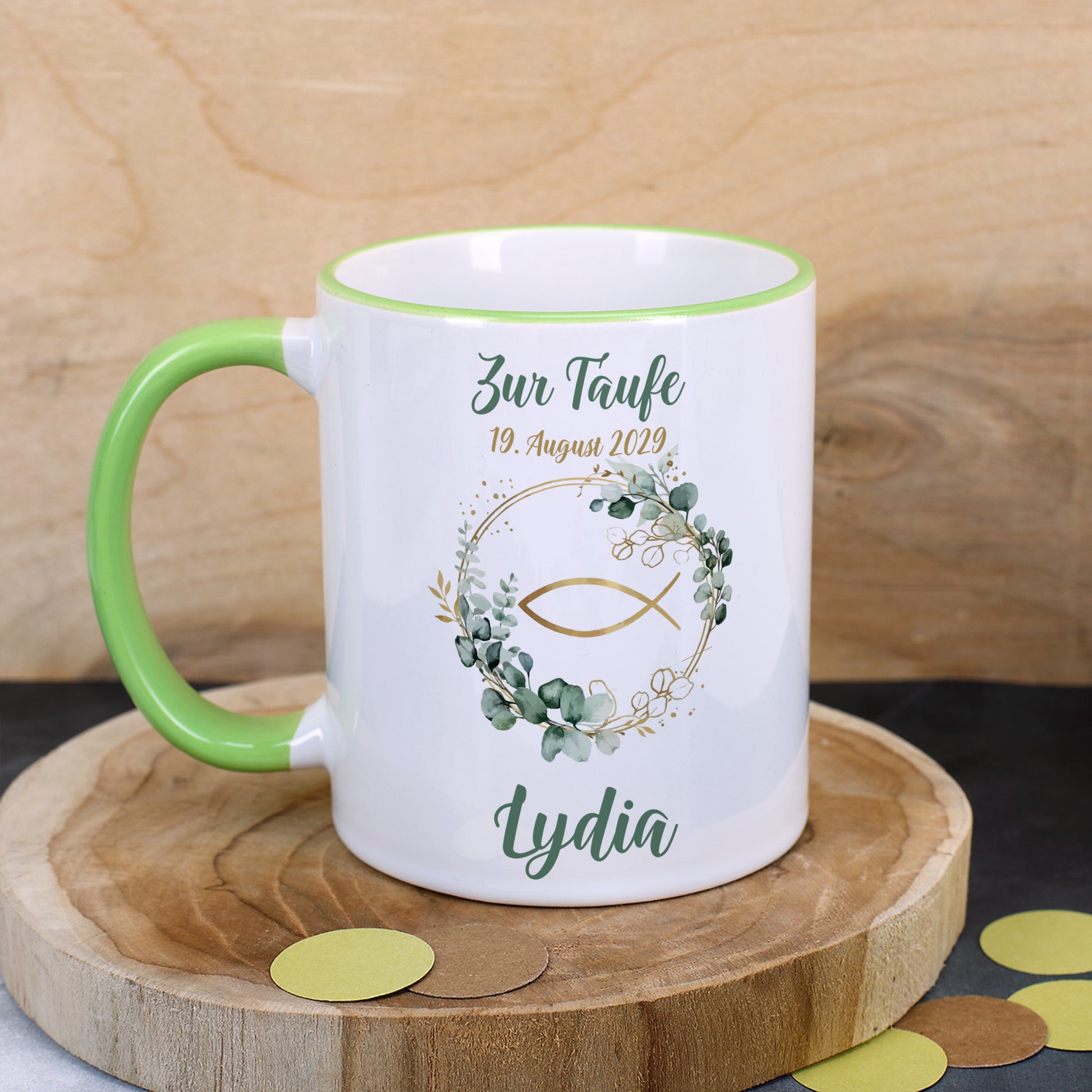 Religiöse Keramiktasse zur Taufe mit Ichthys-Fisch im Eukalyptuskranz, personalisiert mit Name „Lydia“ und Datum, dekorativ inszeniert