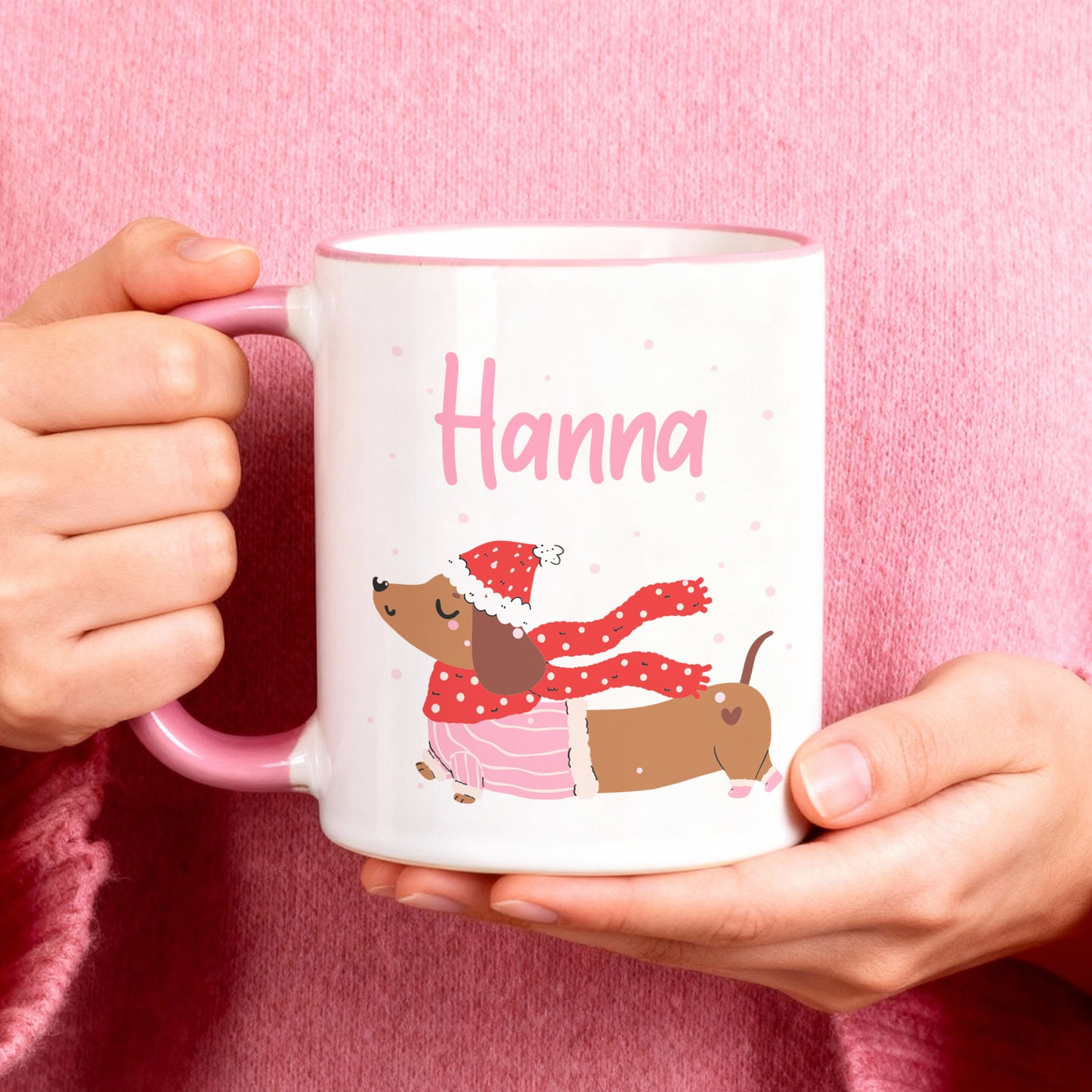 Personalisierte Keramiktasse mit winterlichem Dackel-Motiv und Name, rosa Henkel, gehalten in den Händen