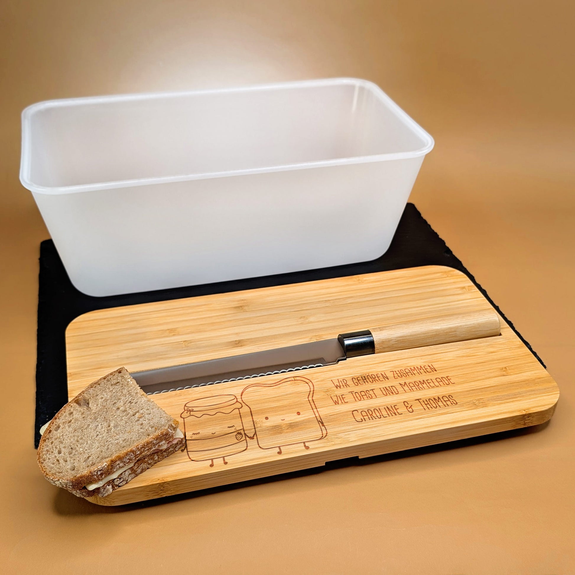 Offener Brotkasten mit Messer und Brot auf Bambus-Schneidebrett