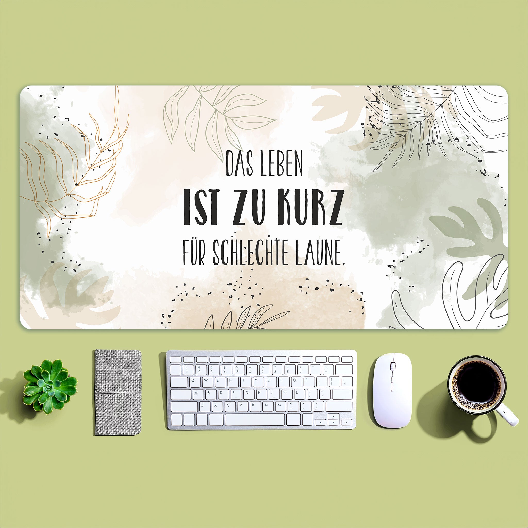 Weißes XXL-Mousepad mit grünbraunem Pflanzen-Motiv und zentriertem Wunschtext – auf grünem Hintergrund mit geordneten Schreibtischutensilien darunter