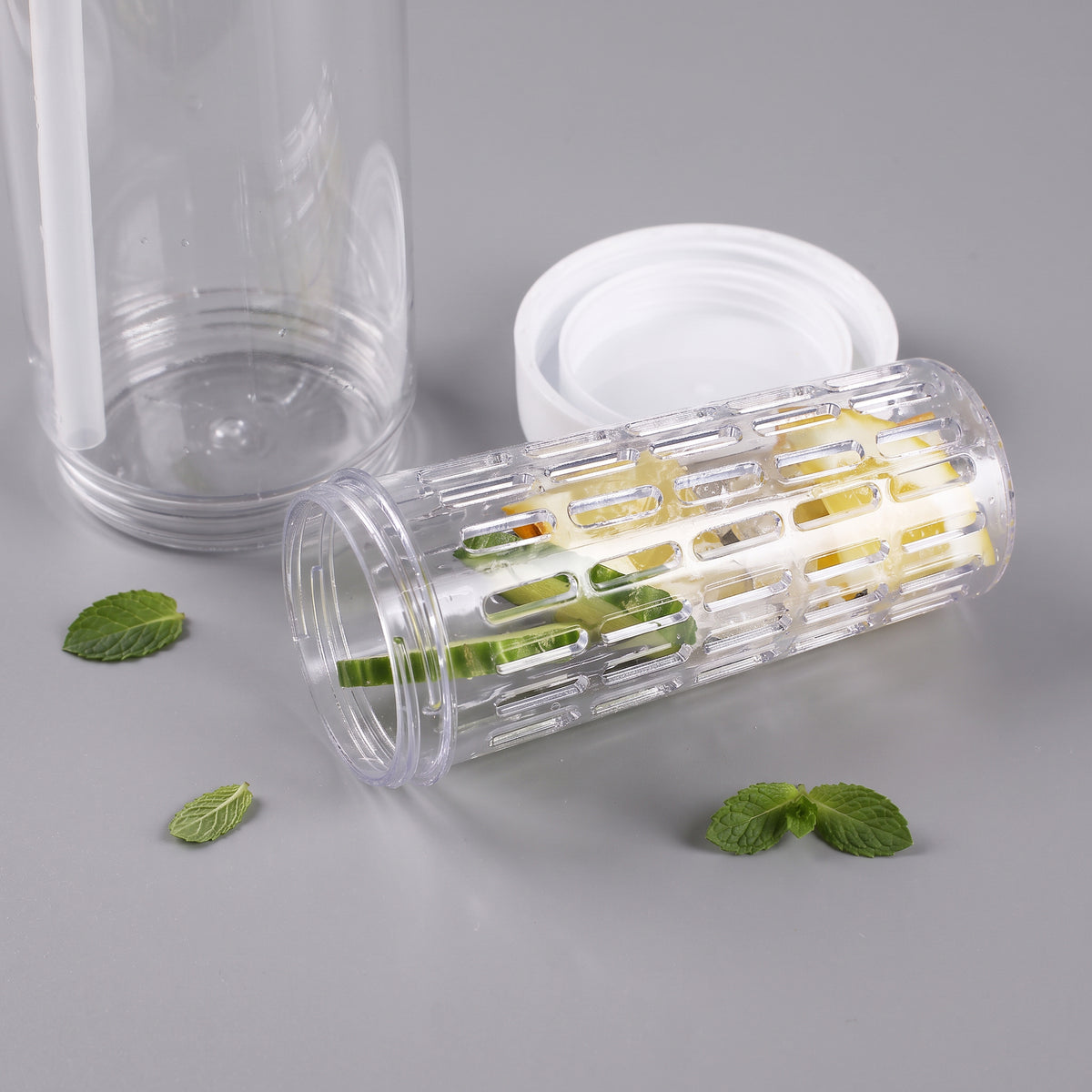 Herausnehmbarer Fruchteinsatz der Trinkflasche mit Zitronen- und Gurkenscheiben neben Flasche und weißem Schraubring