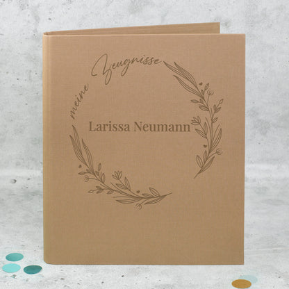 Braune Zeugnismappe aus Leinen mit floralem Lineart-Ring, Aufdruck „meine Zeugnisse“ und personalisiertem Namen „Larissa Neumann“.