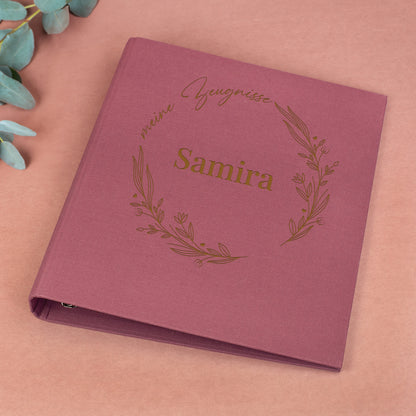 Rosafarbene Zeugnismappe aus Leinen mit floralem Lineart-Ring, Aufdruck „meine Zeugnisse“ und Name „Samira“.