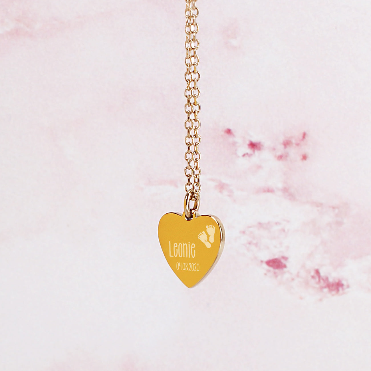 Nahaufnahme der goldenen Leonardo Herzkette zur Geburt mit Name und Datum des Babys graviert