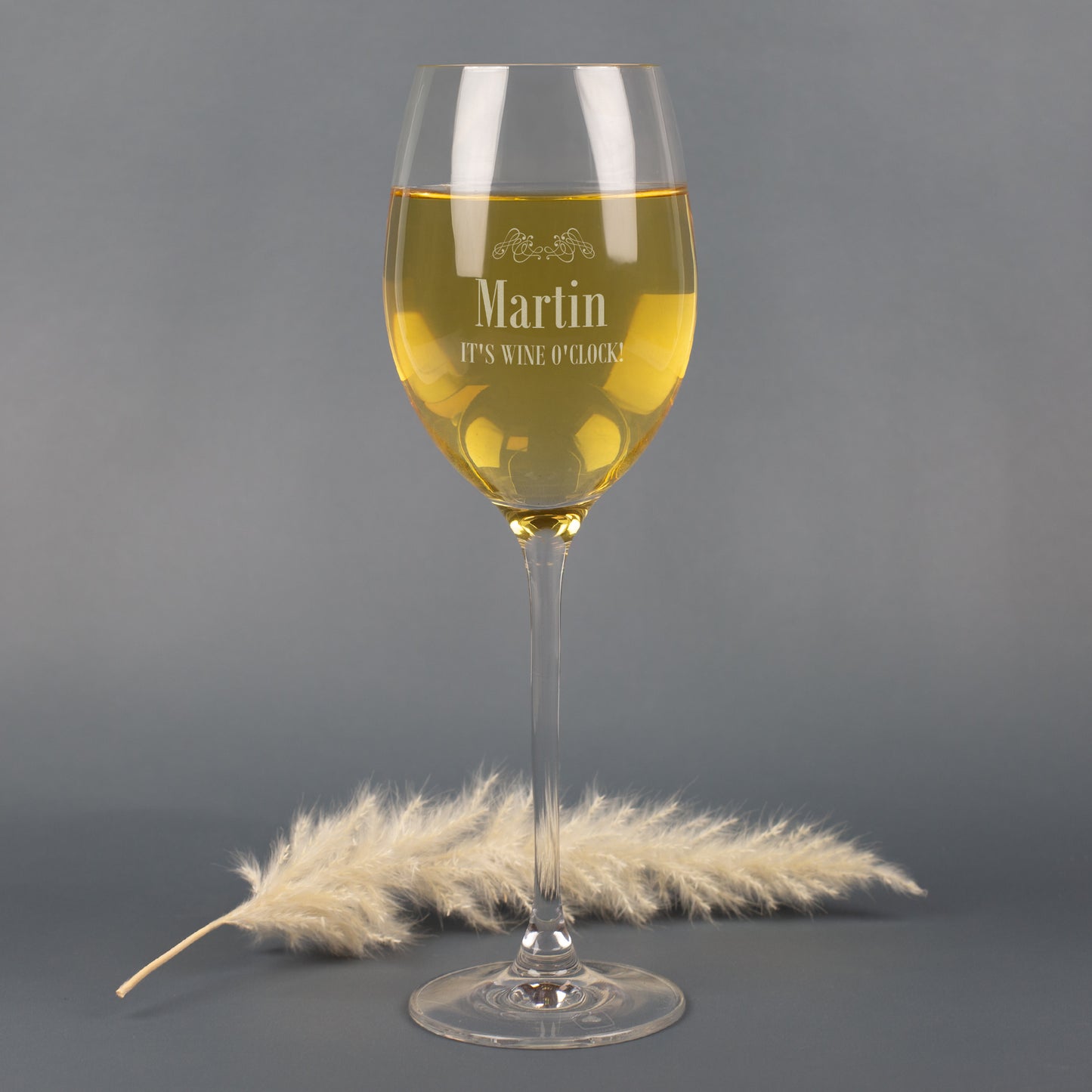 Personalisierbares Leonardo Weißweinglas mit Gravur Martin und Spruch It’s Wine O’Clock, auf grauem Hintergrund mit Pampasgras