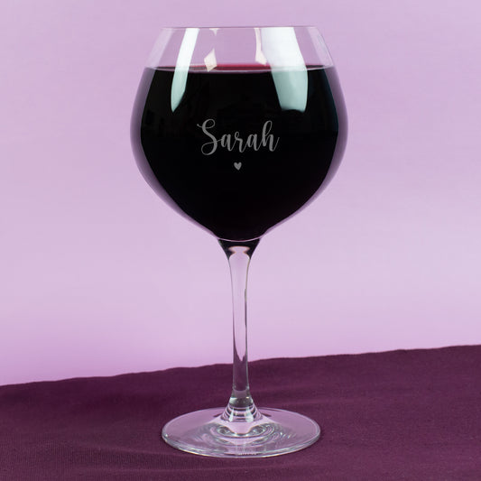 Personalisierte Gravur auf Leonardo Burgunderglas mit Name „Sarah“ und kleinem Herzmotiv – gefüllt mit Rotwein, vor pastellfarbenem Hintergrund, edel und romantisch gestaltet.