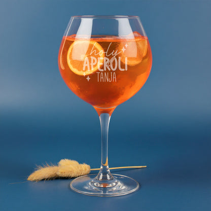Personalisierte Gravur „holy aperoli von Tanja“ auf Leonardo Weinglas, gefüllt mit Aperitifgetränk, Orangenscheiben und Eiswürfeln – modernes Glas mit witzigem Spruch vor blauem Hintergrund.