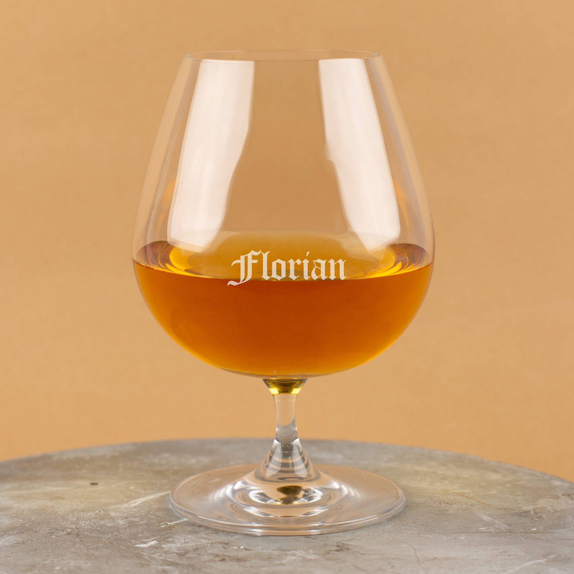 Cognacglas mit Gravur „Florian“ in Frakturschrift – auf grauem Untergrund vor beigefarbenem Hintergrund.